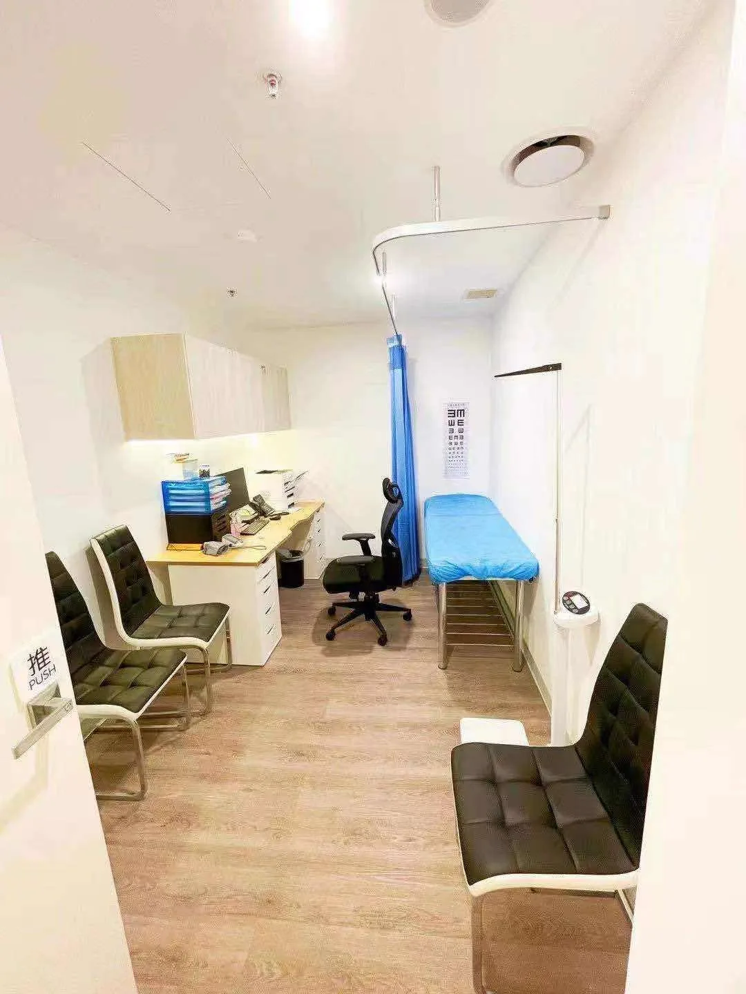 GP consult room with desk, exam bed, eye chart and seating